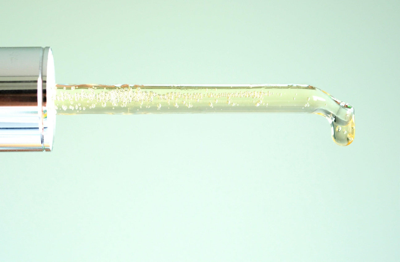 Clear glass dropper with golden facial serum, showcasing product quality and texture.