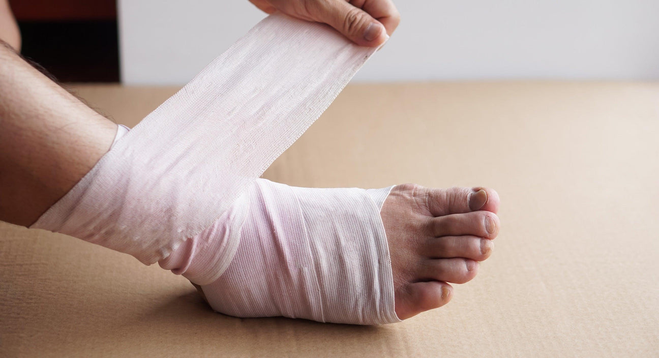Medical professional applying a white elastic bandage to a patient's injured ankle.