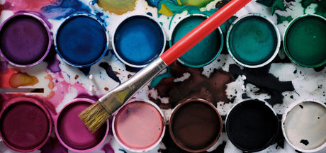 Vibrant watercolor paint palette with a red brush, showcasing diverse colors for creative projects.
