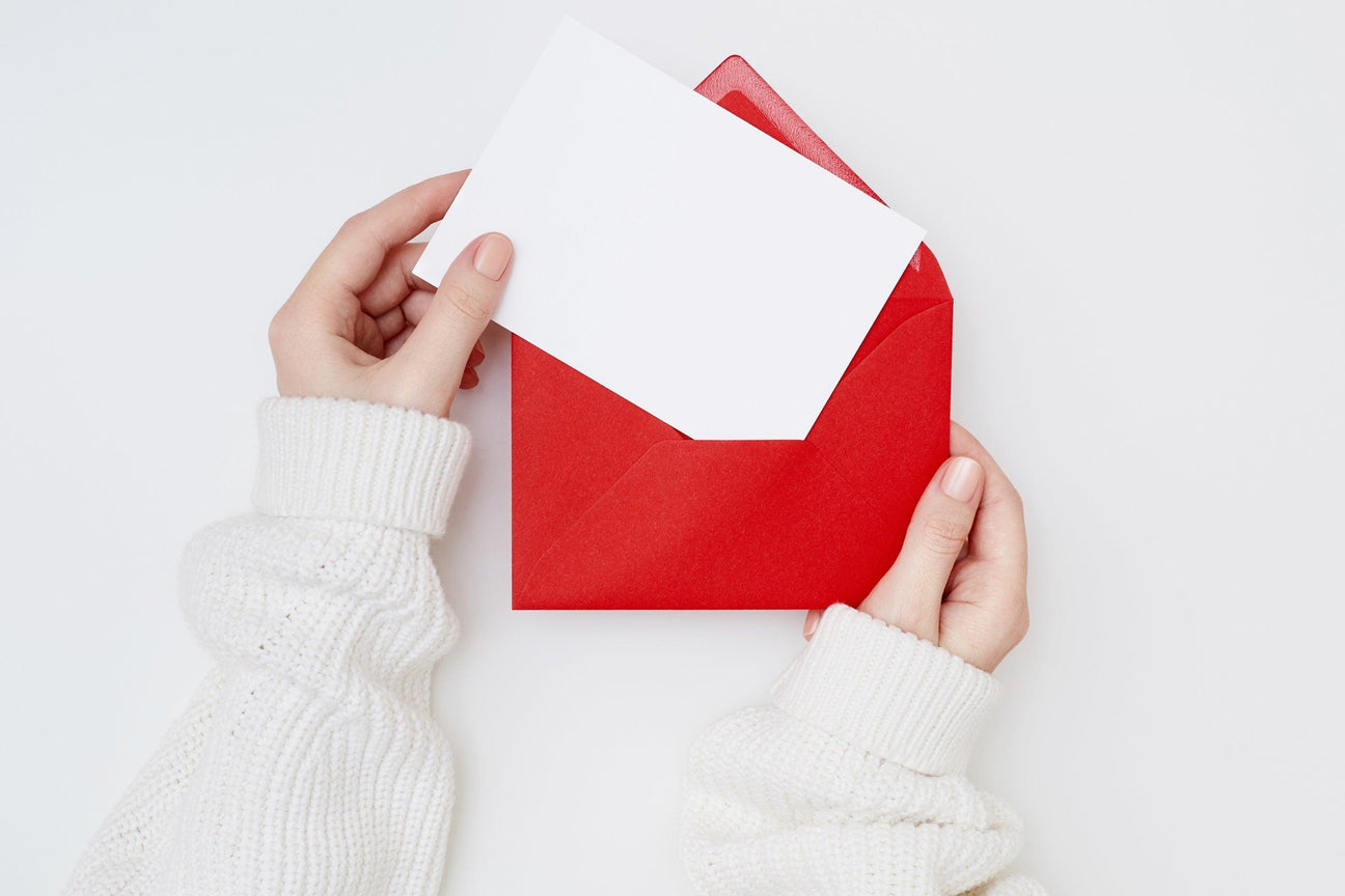 Hands in a white sweater insert a blank card into a vibrant red envelope, ideal for party invitations.