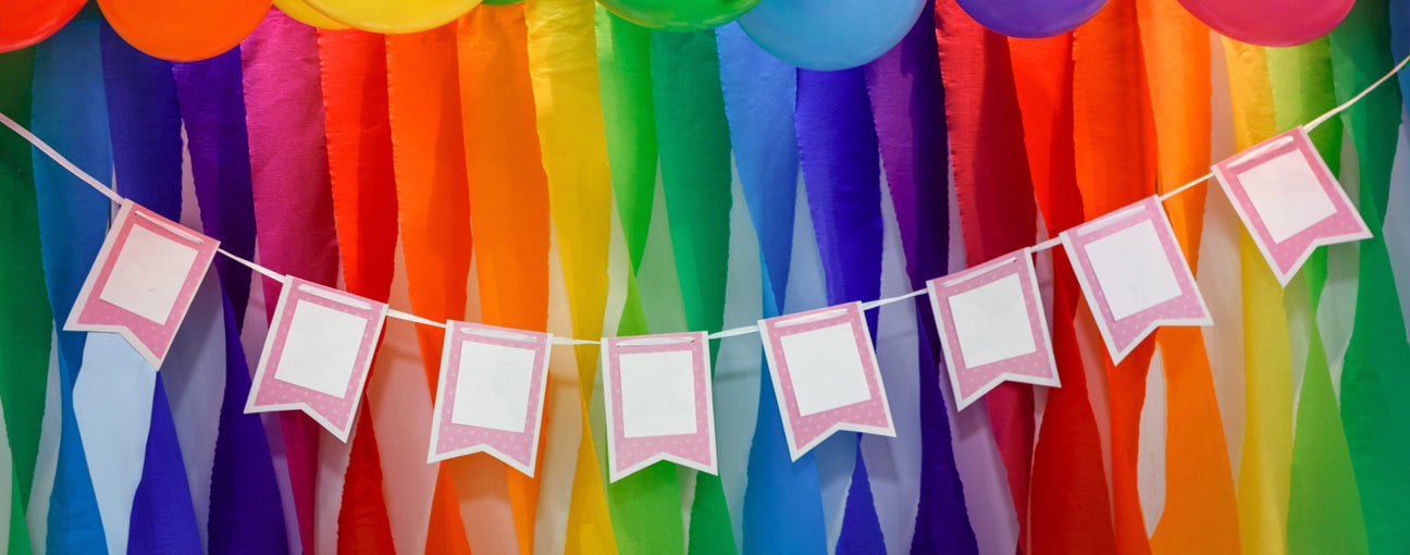 Vibrant rainbow crepe paper streamers, colorful balloons, and a customizable pink banner for festive events.