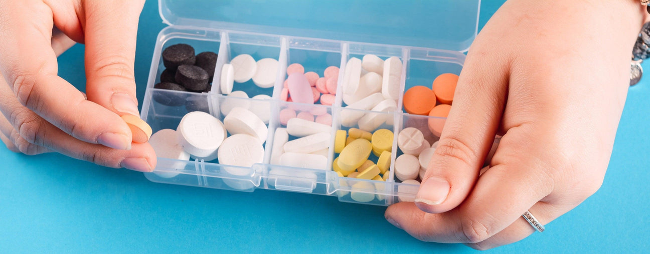 Clear multi-compartment pill organizer with assorted pills, held by hands, ideal for bulk medical supply.