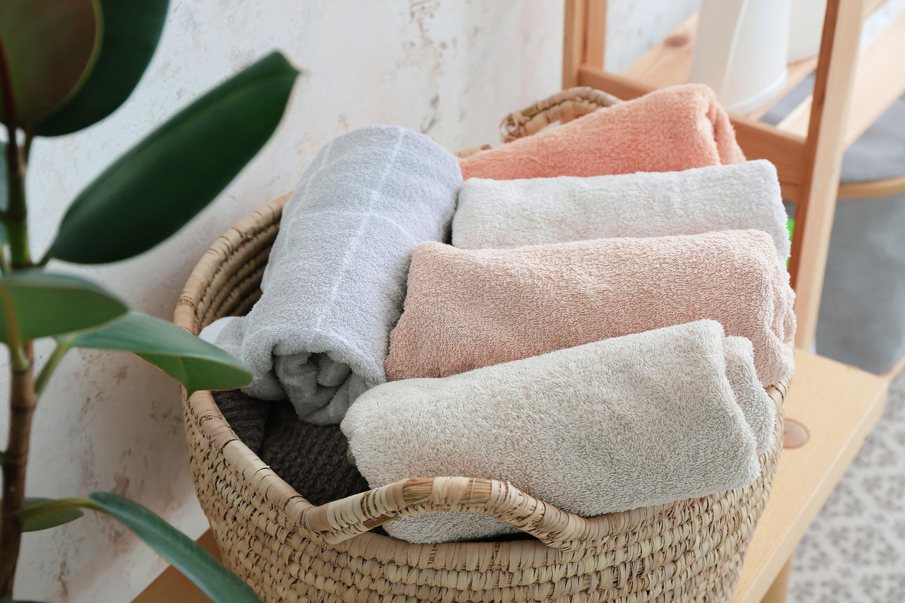Woven basket filled with rolled bath textiles in soft peach, white, and grey, ideal for hospitality.