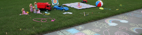 Vibrant summer toys: dolls, truck, car, beach ball, and chalk art on grass and pavement.