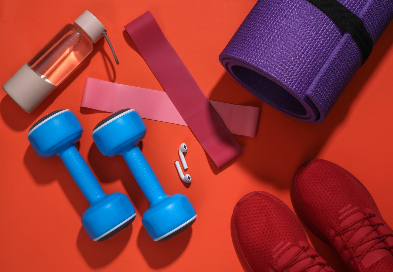 Vibrant fitness collection: blue dumbbells, pink resistance bands, purple yoga mat, water bottle, and red sneakers.